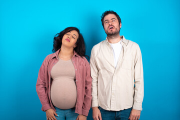 young couple expecting a baby standing against blue background looking sleepy and tired, exhausted...