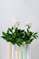 Vertical image.Abstract paper vase and white peonis against white wall.Empy space