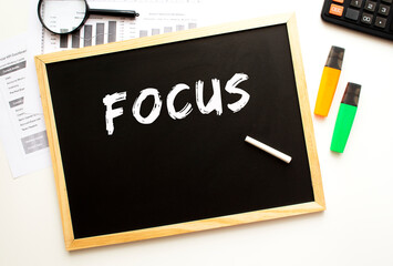 Text FOCUS written in chalk on a slate board. Office desk with office supplies.
