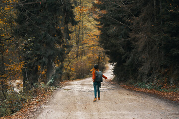 Obraz premium happy travel with a backpack in a warm sweater, trousers and boots walks along the road in the autumn forest