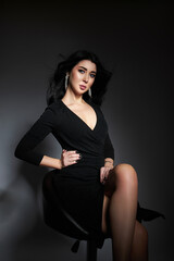 Fototapeta na wymiar Beautiful brunette woman in a black dress poses in the studio. Elegant girl with beautiful natural makeup