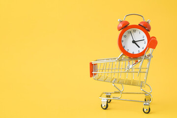 red analog clock on shopping cart with yellow background , payday ,shopping day or sale promotion