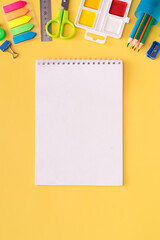 Blank notebook with school supplies on yellow background