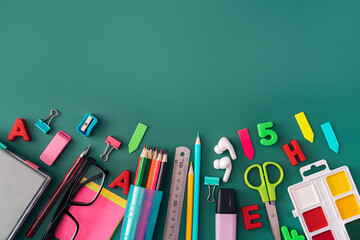 Office stationery, headphones, glasses and paints on green background