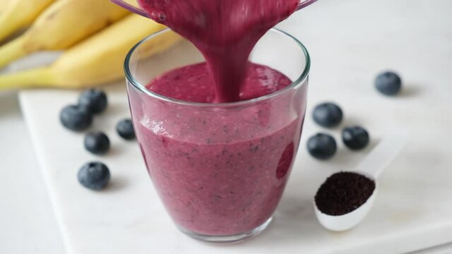 Pouring blueberry smoothie in glass. Thick purple smoothie with acai powder