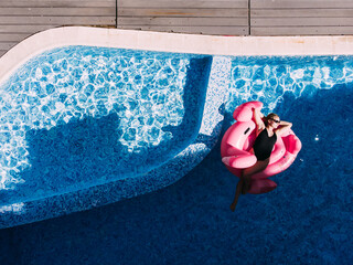 Summer holidays, relaxation. Woman on flamingo pool float in pool, drone aerial view. Enjoying...