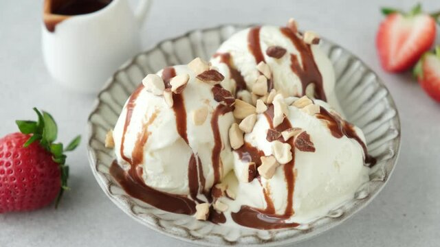 Vanilla ice cream with chocolate sauce. Adding chopped nuts to vanilla ice cream scoops served on dessert plate