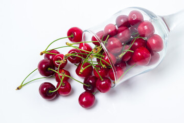 Obraz na płótnie Canvas Red cherries spilled out of the glass on a white background. Sweet cherry with tails. Healthy food