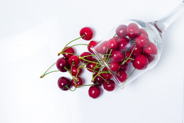 Obraz na płótnie Canvas Red cherries spilled out of the glass on a white background. Sweet cherry with tails. Healthy food