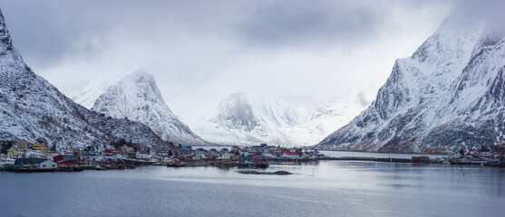 Winter landscape in north Norway: fjord with the little village of Reine against snow covered mountains - obrazy, fototapety, plakaty
