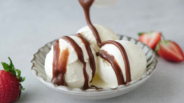Chocolate sauce pouring on vanilla ice cream scoops. Summer dessert. Unhealthy eating, rich in sugar and fat food