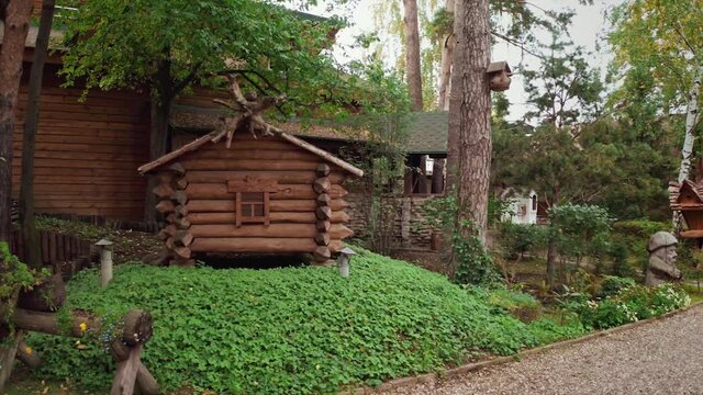 Details of a summer park with traditional russian fairytale wooden houses surrounded by green lawn and trees. Video. A hut on chicken legs or Baba Yaga hut In Slavic folklore.