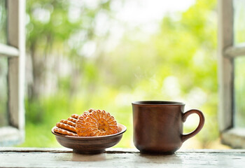 a mug of tea and a plate of cookies stand on the windowsill of an open window against the backdrop of a blurred garden with trees