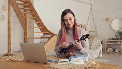 Online learning to play a musical instrument. Young woman learning to play ukulele remotely.