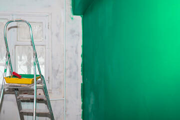 Stepladder, paint tray and roller on the background of a green wall. Copy space