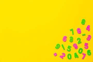 Colored plastic numbers zero, one, two, three, four, five, six, seven, eight, nine in a chaotic order on yellow background with copy space. Wallpaper for notebooks or school market advertising banner