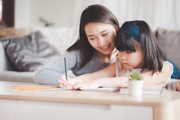 Happy Asian family mother and daughter study or drawing together at home in living room