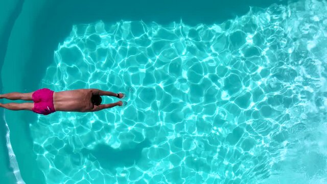 Top down slow motion view of a man diving into the fresh pool water during a hot summer day