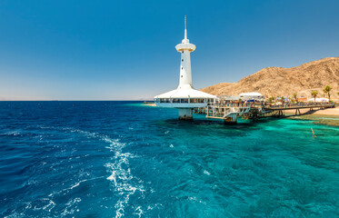 Fototapeta na wymiar Tourist center with building of underwater observatory among coral reefs of the Red Sea and mountains of Sinai, southern beach of Eilat, Israel, Middle East
