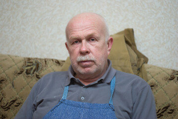 Indoor portrait of a Caucasian senior man looking with pacification while sitting on a sofa.