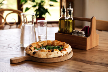 Pizza and water in glass jug on wooden table in vintage style. Italian restaurant background for your design.