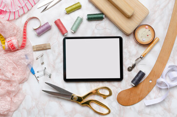 Top view of blank screen of digital tablet, scissors,thread,pins,fabrics,measuring tape,wooden...