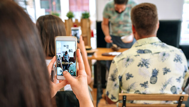 Woman taking photo with mobile to the cook in a cooking workshop. Selective focus on mobile in the foreground
