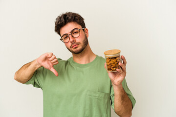 Young caucasian man holding an almond jar isolated on white background showing a dislike gesture,...