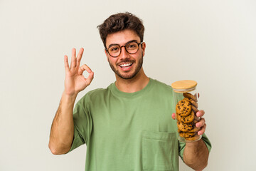 Young caucasian man holding cookies jar isolated on white background cheerful and confident showing...