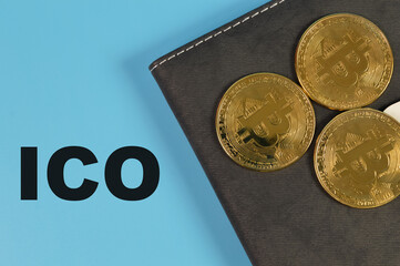 Golden bitcoins and notebook on blue background with text ICO stands for Initial Coin Offering.