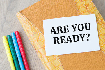 Are you ready inscription on a white card that lies on a notepad on a wooden table