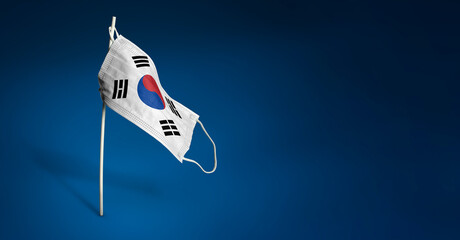 South Korean mask on dark blue background. Waving flag of South Korea painted on medical mask on pole. Concept of The banner of the fight against the epidemic coronavirus COVID-19