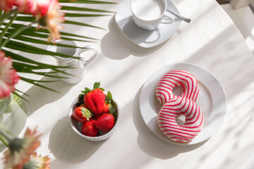 Romantic breakfast in the kitchen with a bouquet of flowers, donuts, coffee and fresh strawberries. Brunch on a sunny day. View from above. Authentic footage from real life