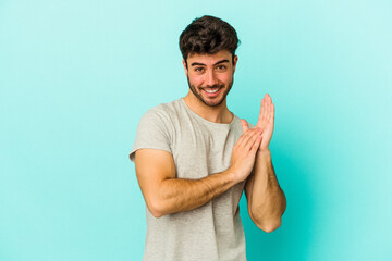 Young caucasian man isolated on blue background feeling energetic and comfortable, rubbing hands...