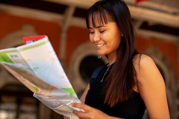 Happy young woman with a city map travelling. Young beautiful female traveler, standing on the street and looking at the map.