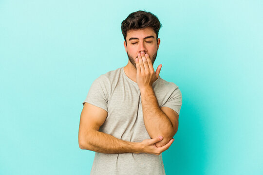 Young caucasian man isolated on blue background yawning showing a tired gesture covering mouth with hand.