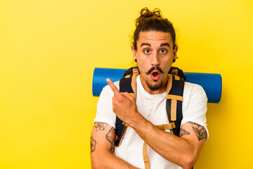 Young caucasian hiker man with long hair isolated on yellow background pointing to the side