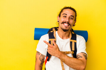 Young caucasian hiker man with long hair isolated on yellow background smiling and pointing aside, showing something at blank space.