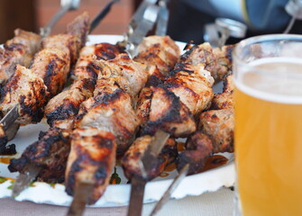 Homemade freshly cooked shish kebab on skewers on the background of the fireplace for frying and a glass of cold beer. Photo of the food.