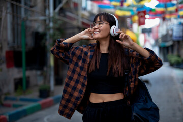 Young smiling woman outdoors. Beautiful woman listening to music while walking through the city.