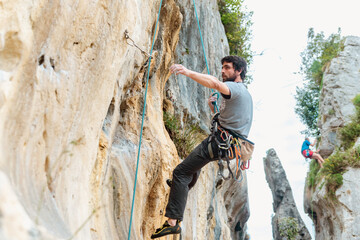 man hanging from a rope descending the rock and releasing the safety hooks. mountain sports and...