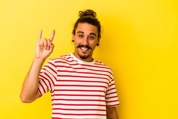 Young caucasian man with long hair isolated on yellow background showing a horns gesture as a revolution concept.