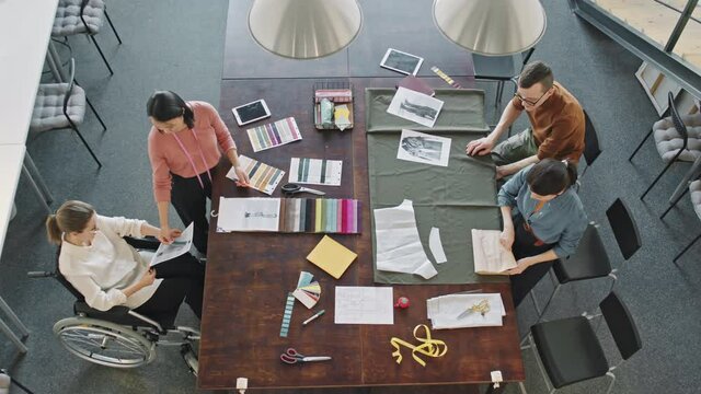 Top view time-lapse shot of diverse team of fashion designers working on garments for new collection in studio
