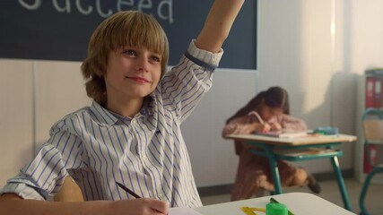 Child raising hand at lesson in auditorium. Smart student answering question