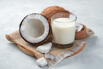 Fresh coconut milk in a glass and coconut on a gray background. Vegetable milk. Side view, close-up.