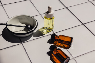 Creative flat lay composition of natural eco-friendly cosmetic products in glass bottles and accessories on a white bathroom tile countertop background. Beauty routine.
