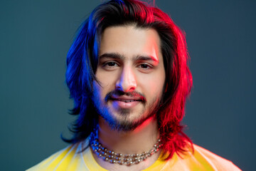 Attractive male portrait. Disco party. Trendy neon light people. Happy man yellow t-shirt beads necklace in blue red vibrant color glow isolated deep ocean.