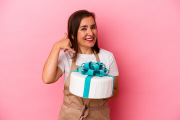 Middle aged pastry chef woman holding a cake isolated on blue background showing a mobile phone call gesture with fingers.