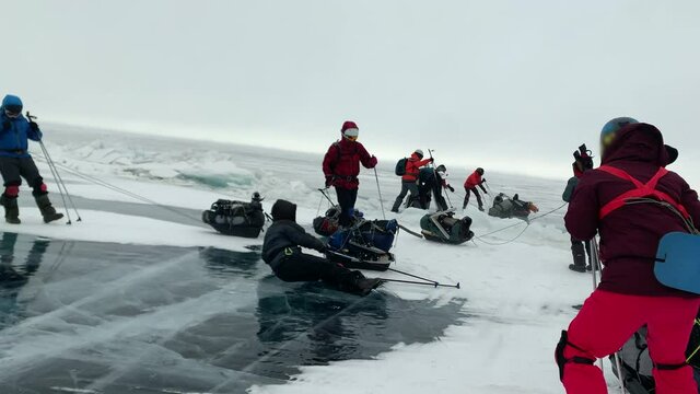 Hurricane wind knocks down tourists traveling on the ice of frozen Lake Baikal in winter. People are blown away and they fall hard and it hurts to turn over on the ice with sledges and backpacks with 