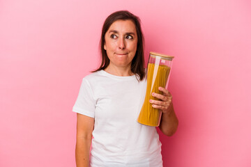 Middle age caucasian woman holding a pasta jar isolated on pink background confused, feels doubtful and unsure.